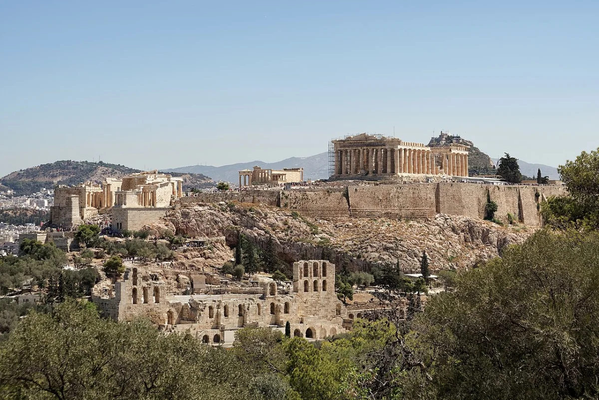 The Acropolis of Athens with the Parthenon on its rock, seen across trees from a hill to the south-west.