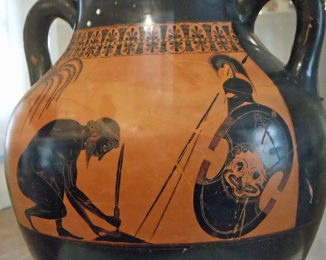 A black-figure vase: a warrior crouches, planting a sword in the ground; his shield and helmet stand by.