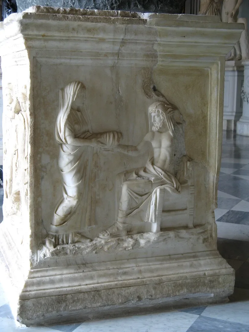 A marble base with a relief of a woman offering a wrapped object to a seated figure.