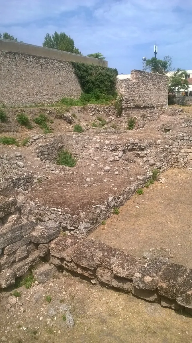 Excavated stone foundations beside a modern wall in the town of Thebes.