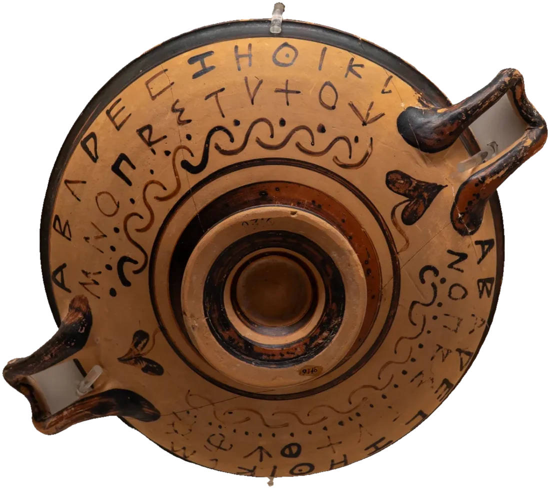 A shallow two-handled cup seen from above, the Greek alphabet painted in black letters round its rim.