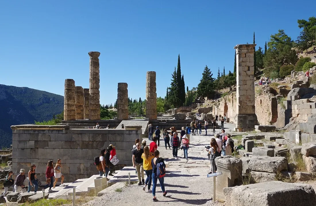 Columns and foundations of a temple on a mountain slope, visitors on the path.