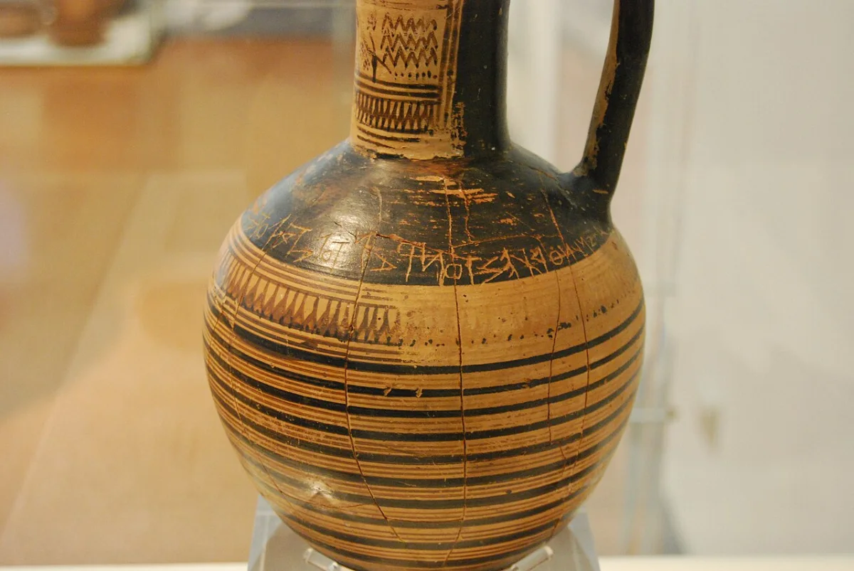A Geometric wine jug with bands of painted decoration; a line of letters is scratched round its shoulder.