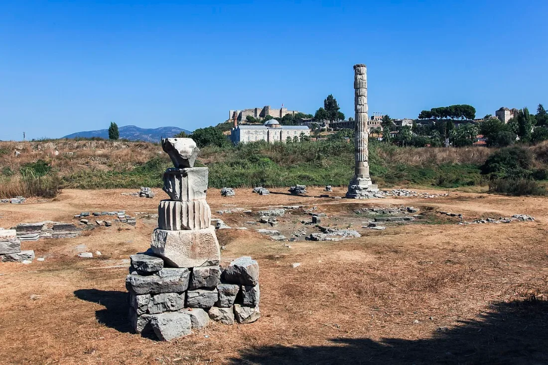 A single reconstructed column among ruins, a mosque and a castle on the hill behind.