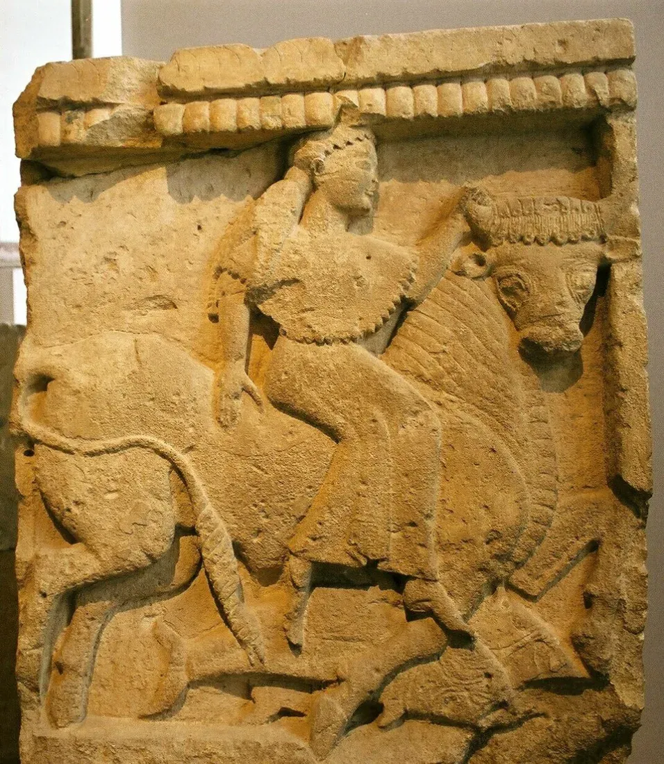 A stone relief of a woman riding a bull over the sea.