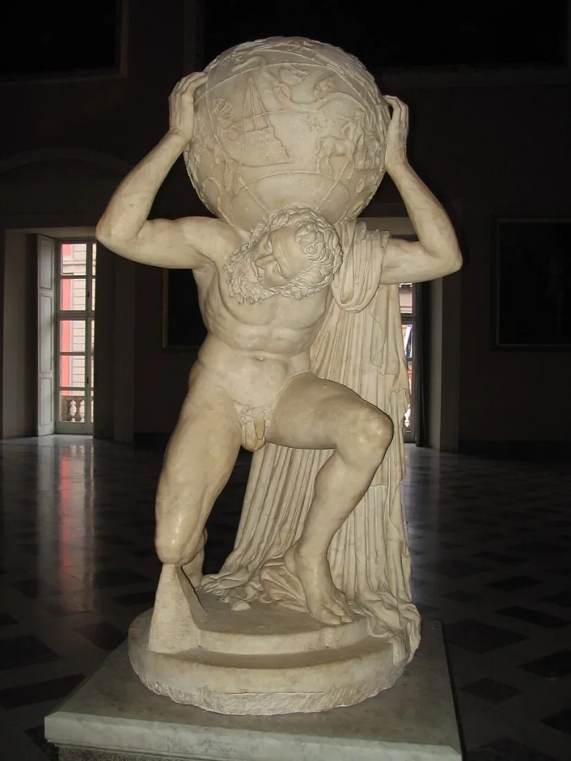 A marble statue of a kneeling man carrying a large globe on his shoulders.