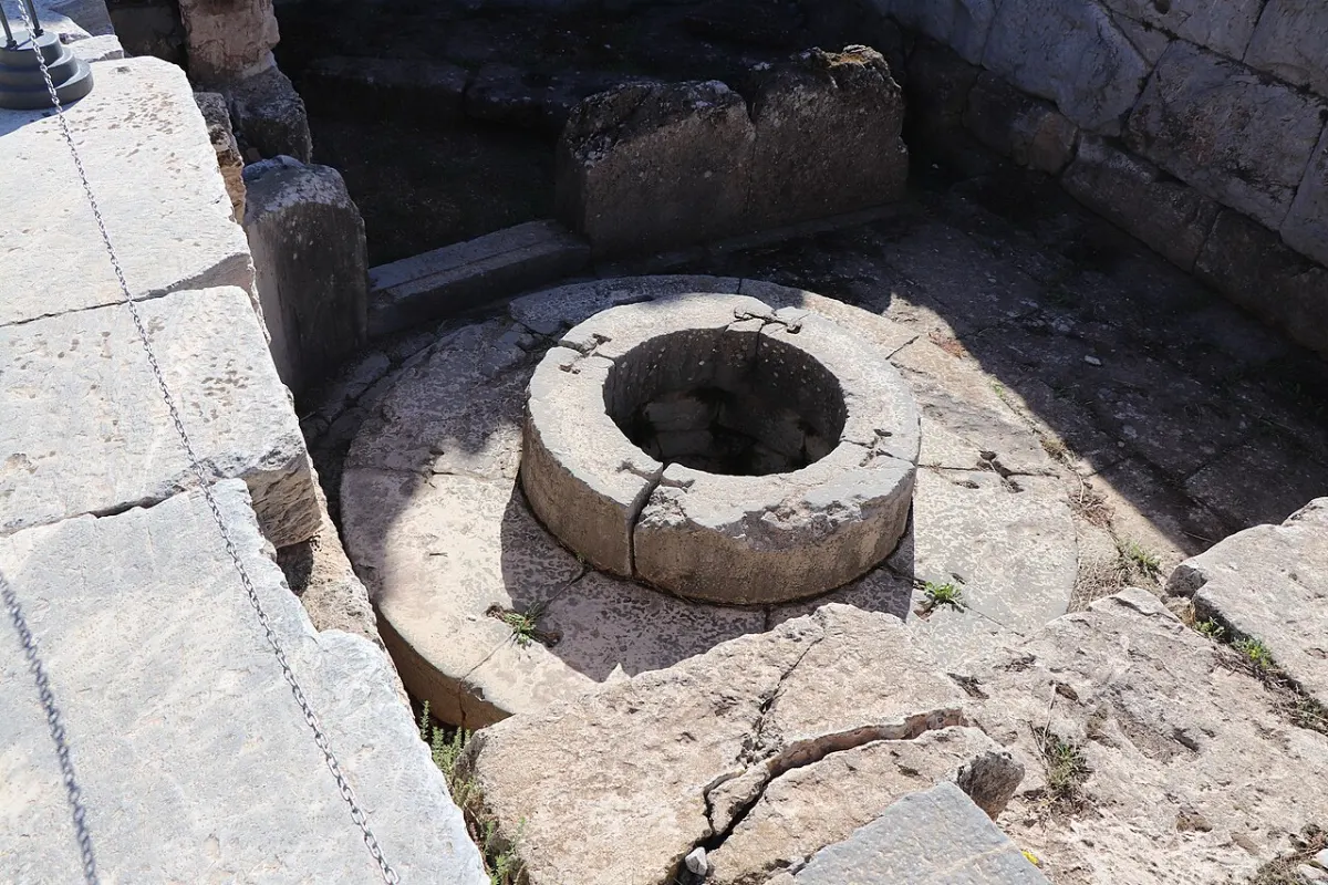 A round stone well-head set in an ancient paved area among ruins.