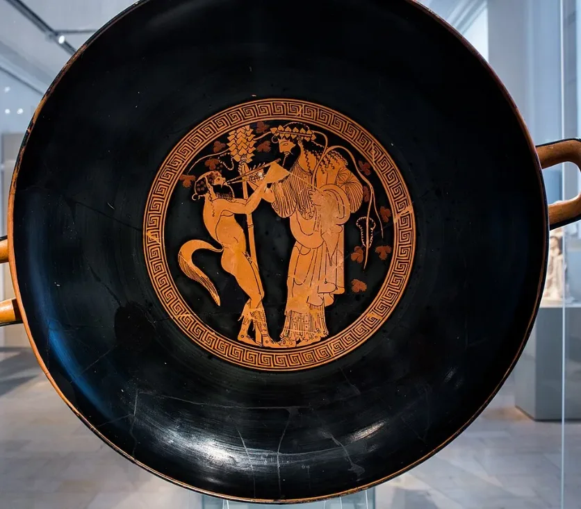 A cup seen from above: in the centre a satyr plays pipes before Dionysus.
