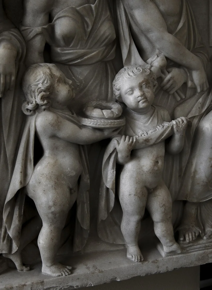 Marble relief: two small boys carry a casket and a robe, among taller draped figures.