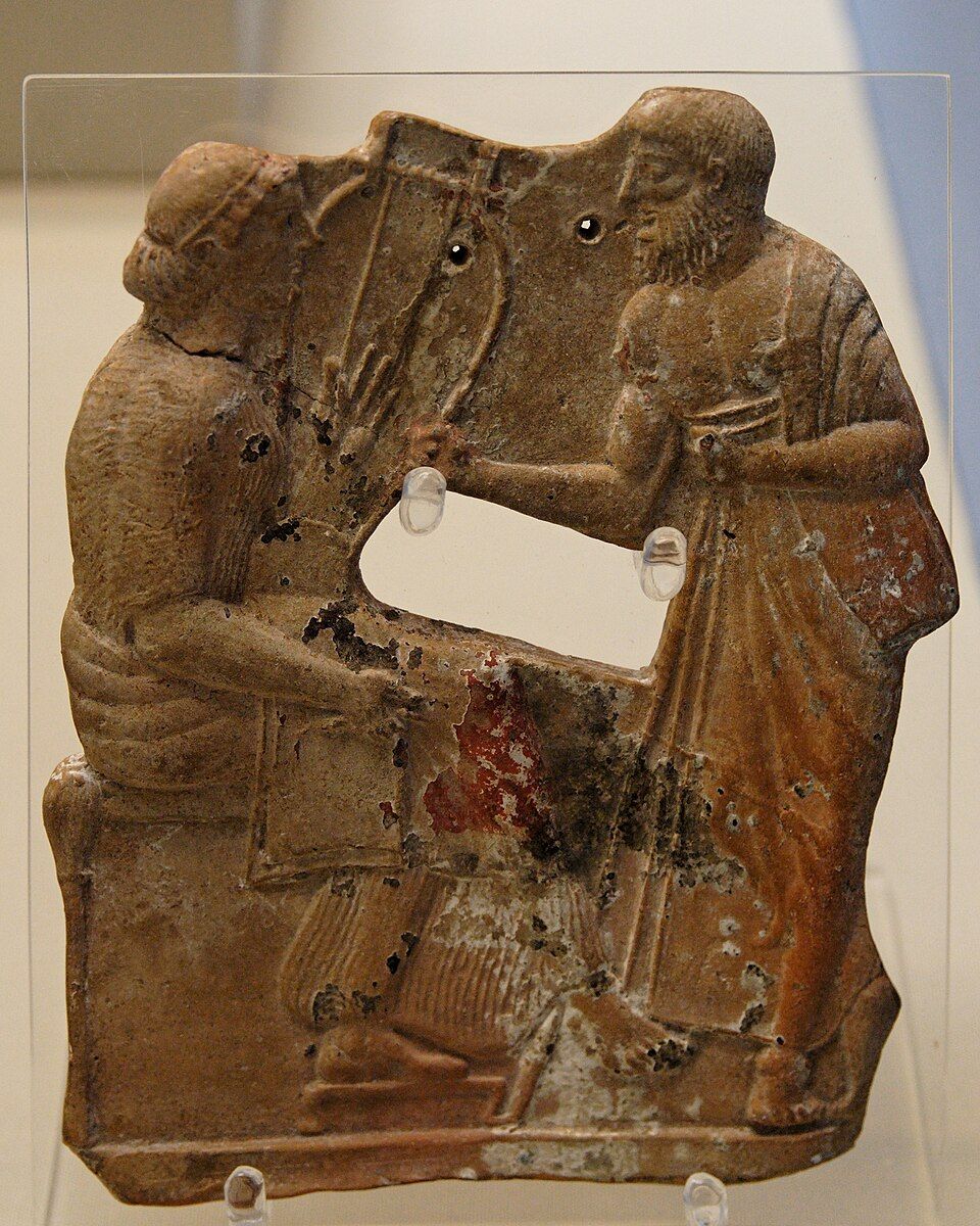 Painted terracotta relief: a seated figure holding a barbitos faces a standing figure.