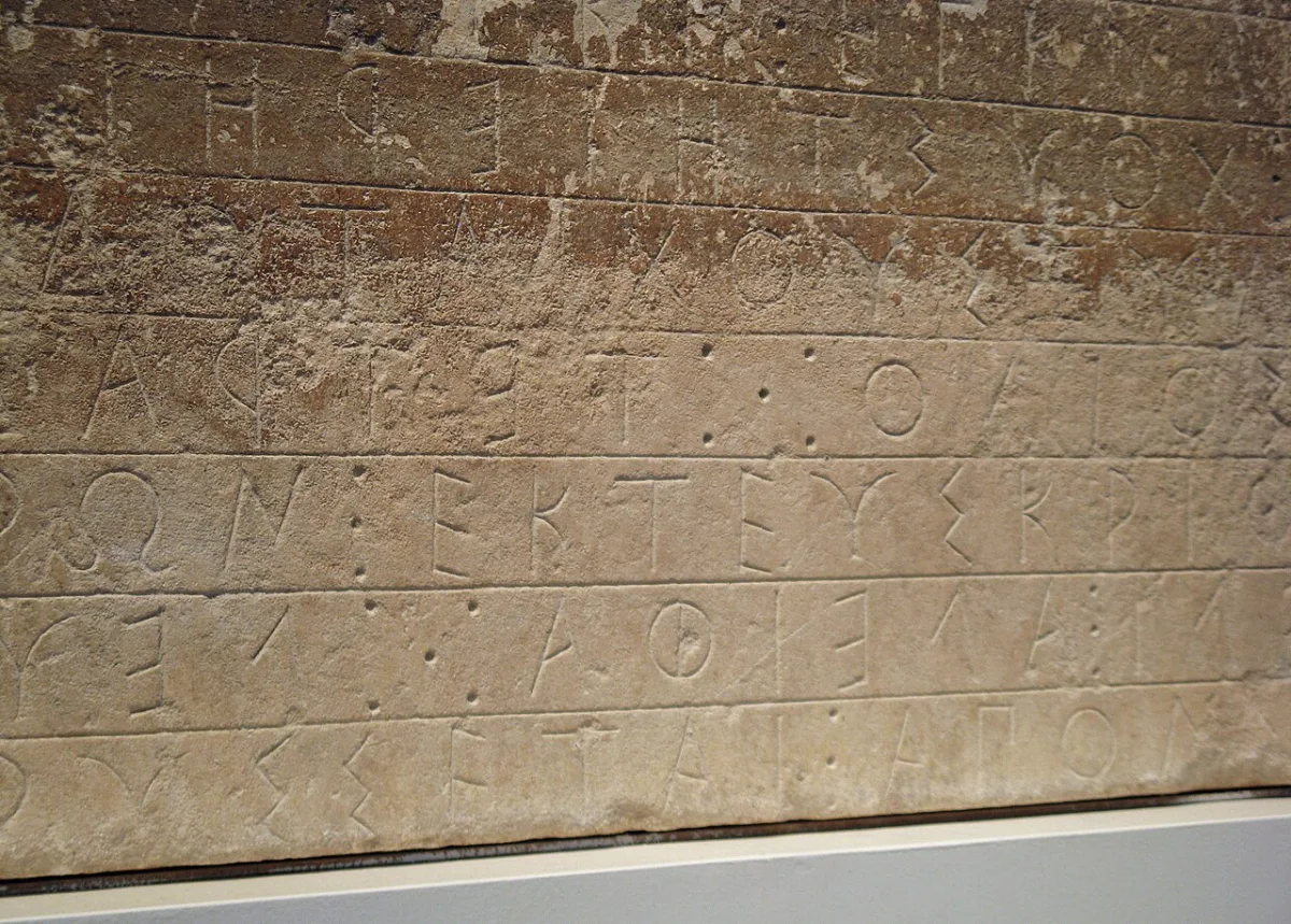 Close view of a weathered marble block inscribed with lines of archaic Greek letters.