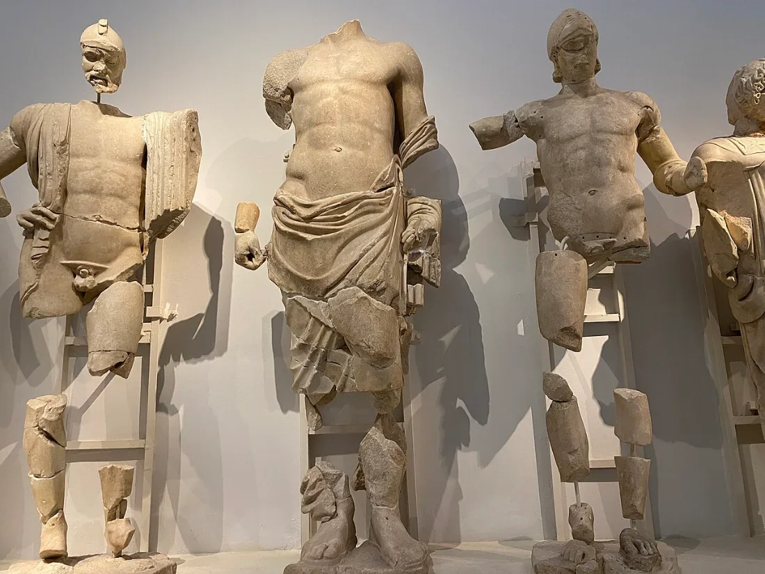 Marble statues of standing men, the central one taller, in a museum gallery.