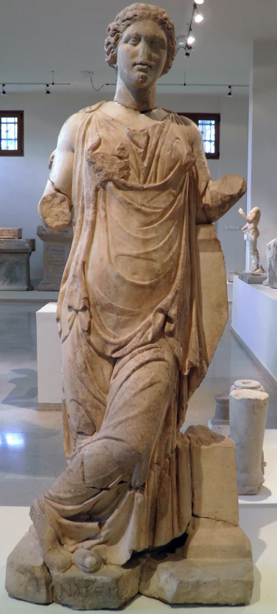 Marble statuette of a draped young woman standing, one arm extended.