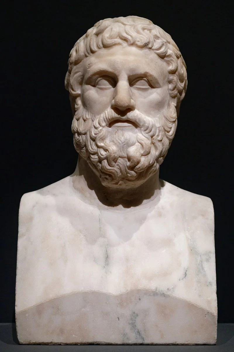 Marble portrait herm of a bearded man with thick curly hair.