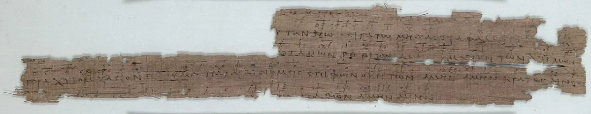 A long narrow strip of papyrus with five lines of Greek capitals, small signs written above them.