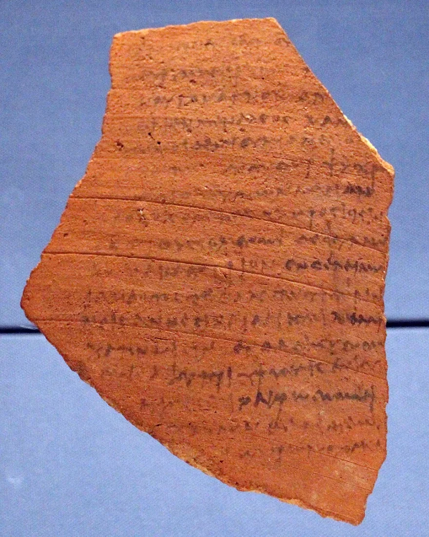 A reddish potsherd covered with lines of faded Greek handwriting.