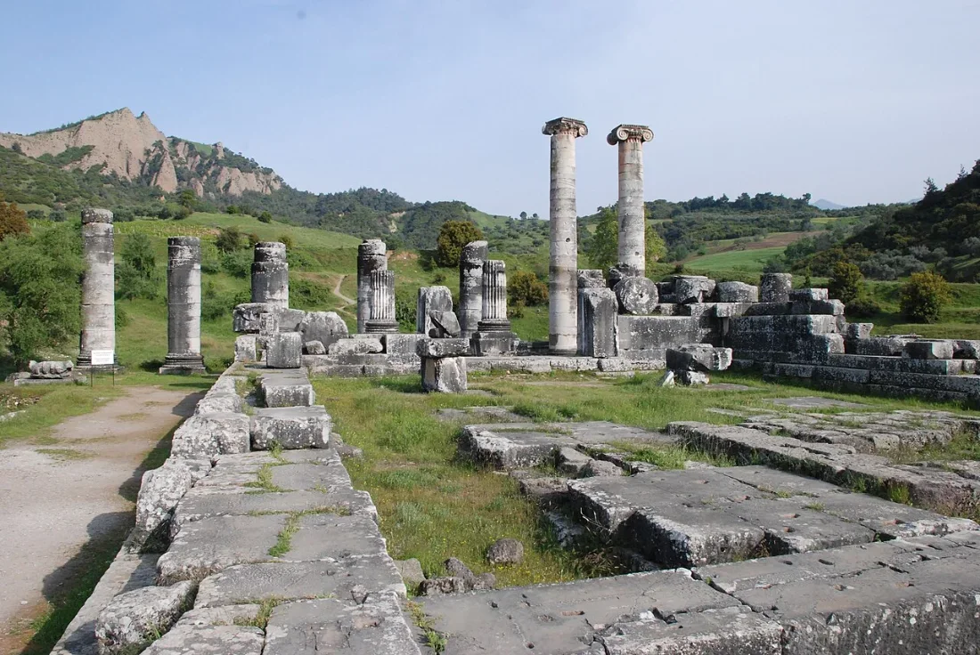 Two standing columns and the foundations of a large temple in green countryside.
